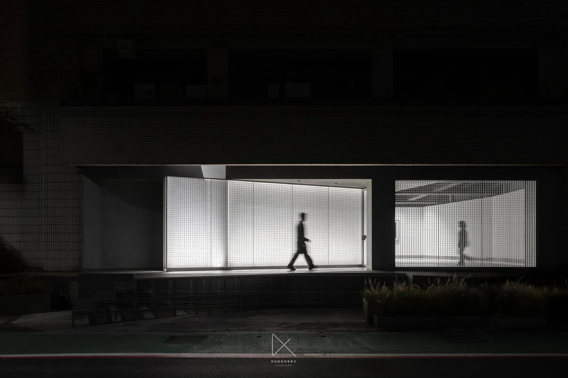 夜裡從街上望向 AXIS Gallery,發光的網格屏是整條街唯一的光,一個人影正走過